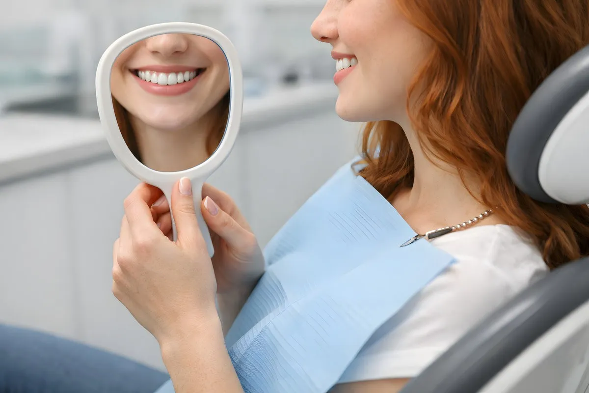 Woman admiring her smile in a mirror after dental bonding treatment