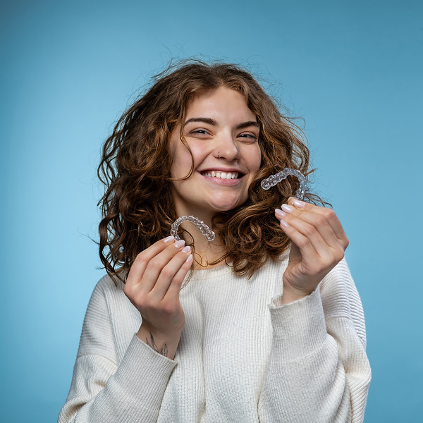 A woman is holding Invisalign clear aligners and smiling