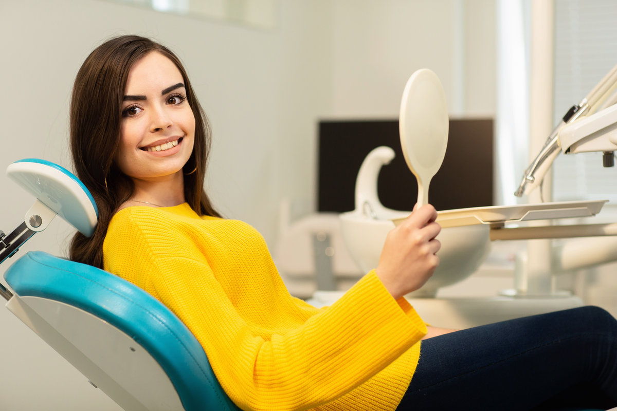 Young happy woman client looking at the mirror with toothy smile at the dental office Young happy woman client looking at the mirror with toothy smile at the dental office.