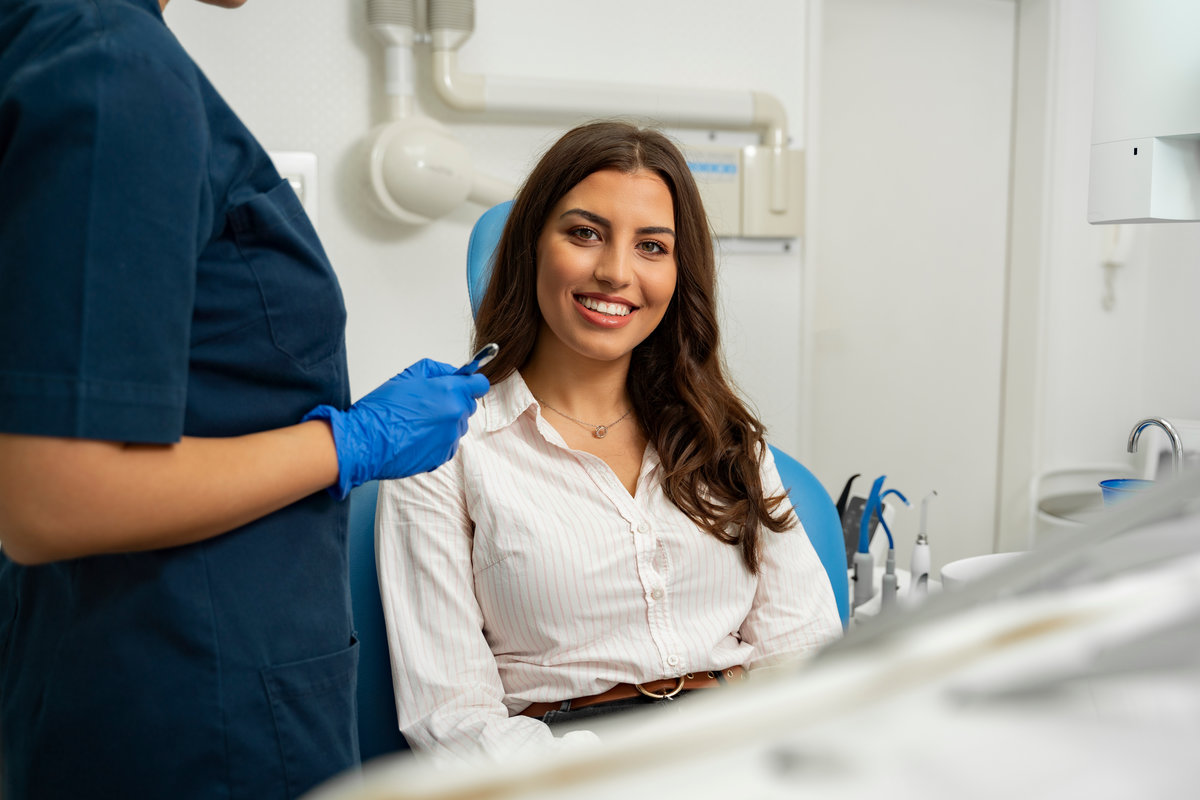 Satisfied patient sitting in dentist chair. Gorgeous young woman in dental clinic smiling from a chair next to dentist Satisfied patient sitting in dentist chair. Gorgeous young woman in dental clinic smiling from a chair next to dentist