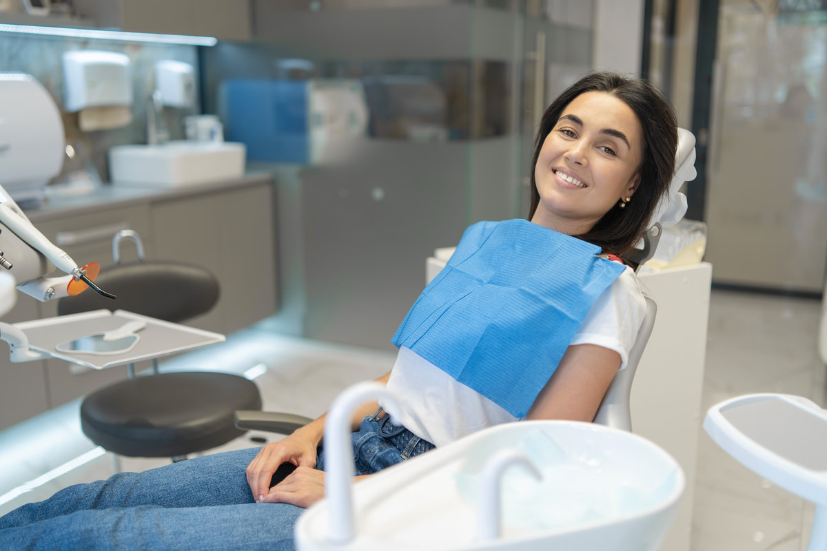 Pretty brunette happy female patient sitting in the chair at dental clinic. Pretty brunette happy female patient sitting in the chair at dental clinic
