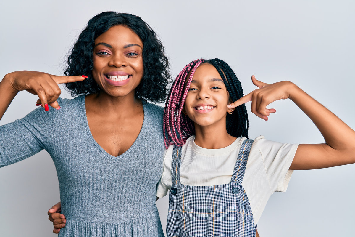 Beautiful african american mother and daughter wearing casual clothes and hugging smiling cheerful showing and pointing with fingers teeth and mouth. dental health concept. Beautiful african american mother and daughter wearing casual clothes and hugging smiling cheerful showing and pointing with fingers teeth and mouth. dental health concept.